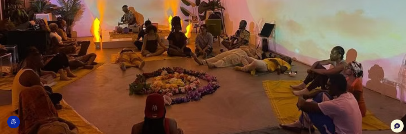 Participants sharing a ceremony around a circle of flowers in a warmly lit community space.